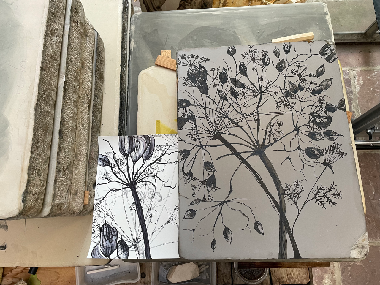 Auf dem Bild sind eine weißhaarige Frau und ein dunkelhaariger Junge zu sehen, vor sich auf dem Tisch eine Linolschnittplatte, die das Gesicht einer Mangafigur zeigt. Der Junge hält einen mehrfarbigen Abdruck des Motivs auf Papier in der Hand.