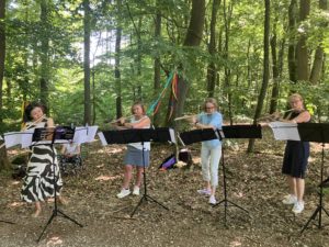 Auf dem Bild ist das Flötenensemble der Musikschule Friedrichsdorf beim Spiel im Wald zu sehen.